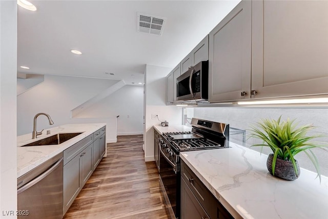 kitchen with sink, gray cabinetry, light hardwood / wood-style flooring, appliances with stainless steel finishes, and light stone countertops