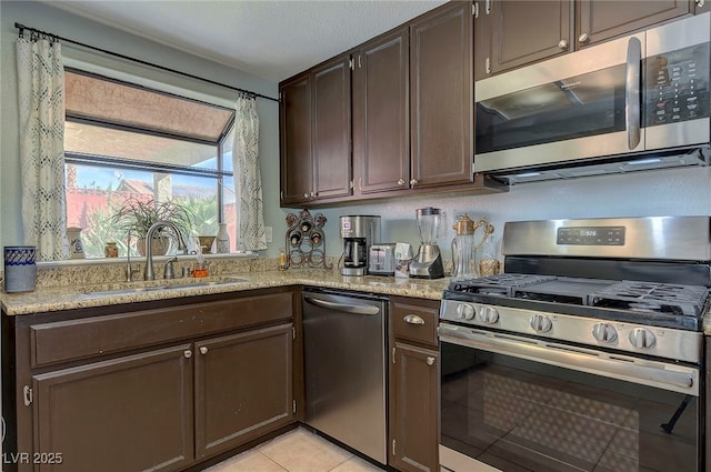 kitchen featuring light stone counters, sink, dark brown cabinets, and appliances with stainless steel finishes