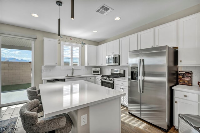 kitchen with stainless steel appliances, white cabinetry, and hanging light fixtures