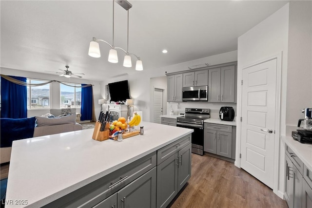 kitchen featuring pendant lighting, ceiling fan, appliances with stainless steel finishes, gray cabinetry, and wood-type flooring