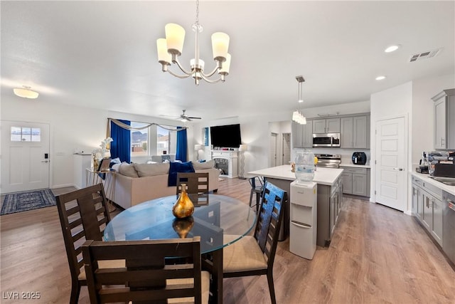 dining space with sink, ceiling fan with notable chandelier, and light hardwood / wood-style flooring