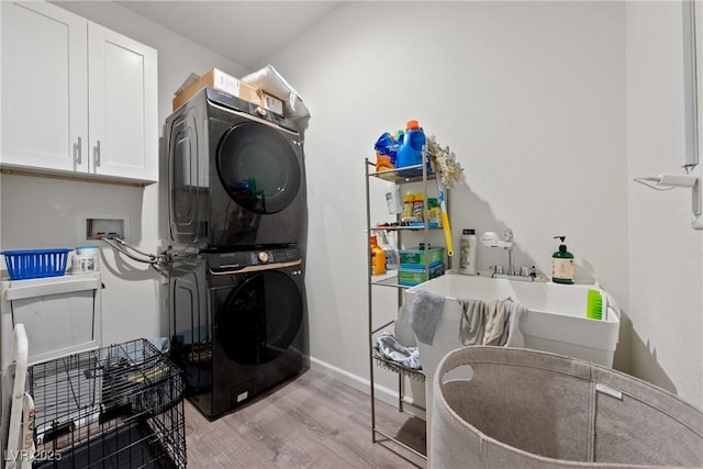 clothes washing area with cabinets, light hardwood / wood-style floors, and stacked washer and clothes dryer