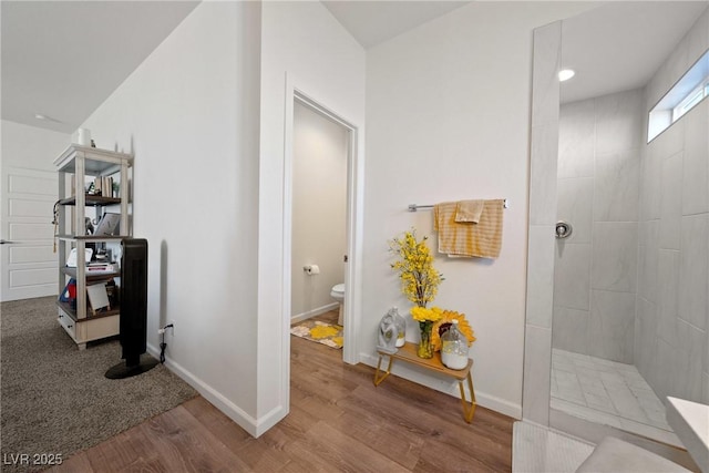 bathroom with hardwood / wood-style flooring, a tile shower, and toilet