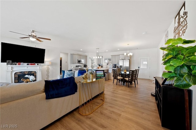 living room with ceiling fan with notable chandelier and light wood-type flooring