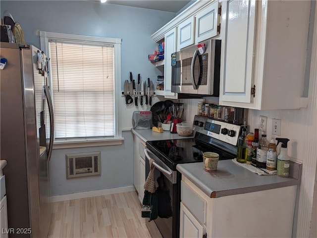 kitchen with white cabinetry, appliances with stainless steel finishes, heating unit, and light wood-type flooring