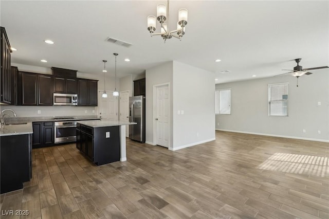 kitchen with sink, light stone counters, a center island, pendant lighting, and stainless steel appliances