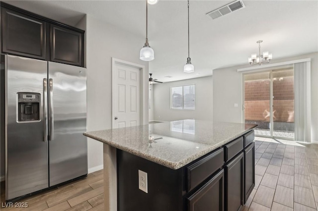 kitchen with a center island, stainless steel fridge with ice dispenser, hanging light fixtures, ceiling fan, and light stone countertops