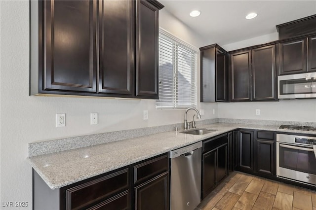 kitchen featuring appliances with stainless steel finishes, sink, dark brown cabinetry, light stone countertops, and light wood-type flooring