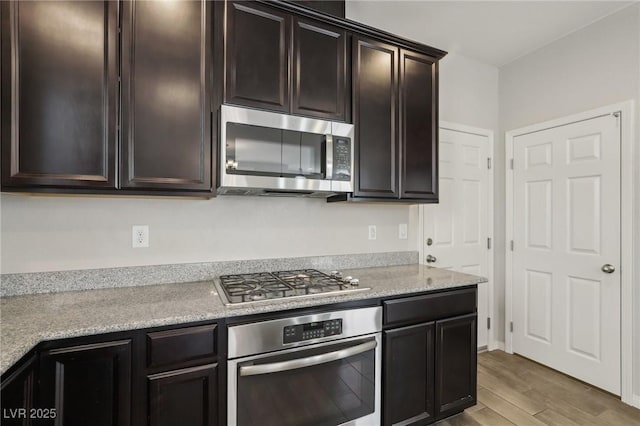 kitchen with dark brown cabinetry, appliances with stainless steel finishes, light stone counters, and light hardwood / wood-style flooring