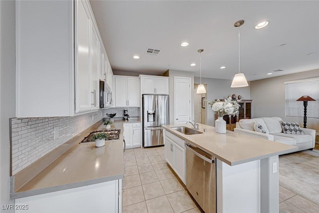 kitchen featuring appliances with stainless steel finishes, pendant lighting, sink, white cabinets, and a center island with sink