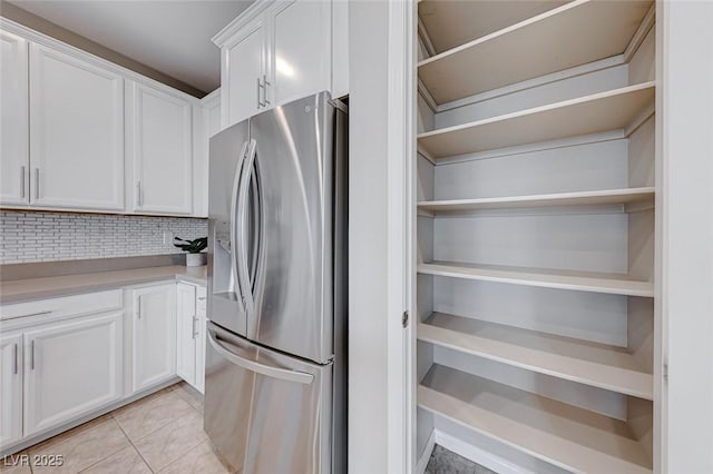 kitchen featuring light tile patterned floors, stainless steel fridge with ice dispenser, decorative backsplash, and white cabinets