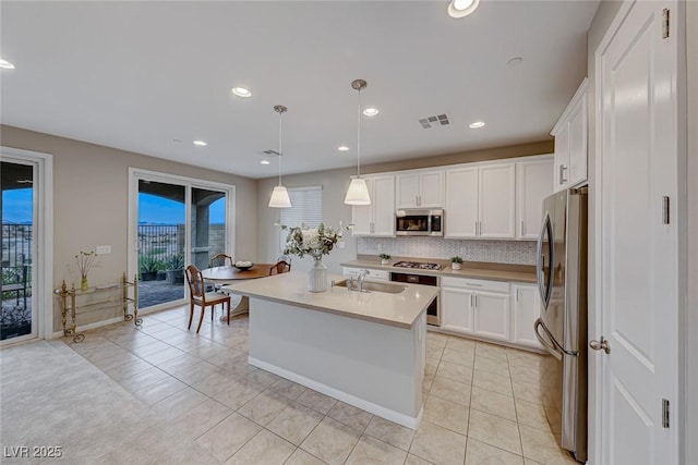 kitchen featuring decorative light fixtures, white cabinetry, backsplash, a kitchen island with sink, and stainless steel appliances