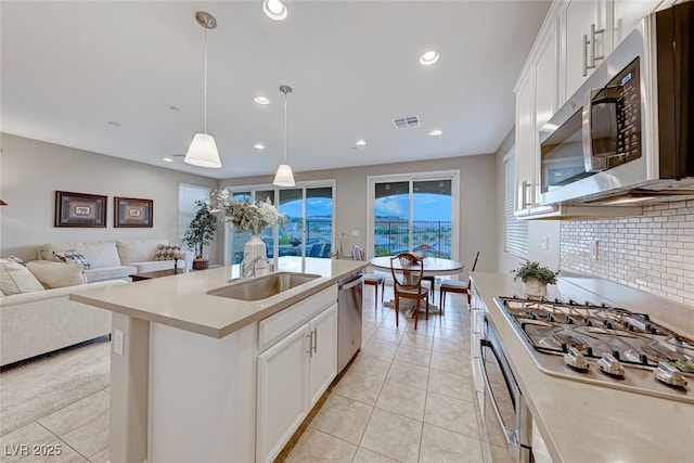 kitchen with sink, hanging light fixtures, stainless steel appliances, a kitchen island with sink, and white cabinets