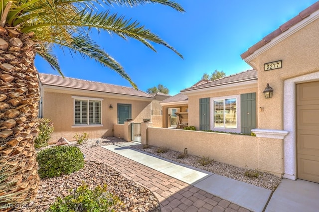 doorway to property featuring a garage, a tile roof, fence, a gate, and stucco siding