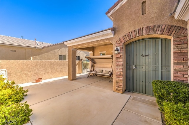 property entrance with a patio area, fence, and stucco siding