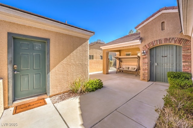 doorway to property with a patio, brick siding, fence, and stucco siding