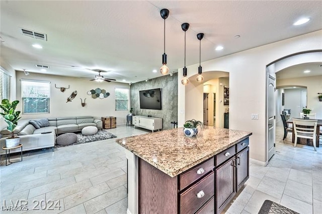 kitchen featuring pendant lighting, ceiling fan, dark brown cabinets, a center island, and light stone countertops