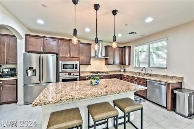 kitchen featuring wall chimney exhaust hood, appliances with stainless steel finishes, a center island, and hanging light fixtures