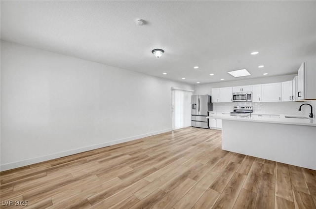 kitchen with tasteful backsplash, a skylight, light wood-type flooring, appliances with stainless steel finishes, and white cabinets