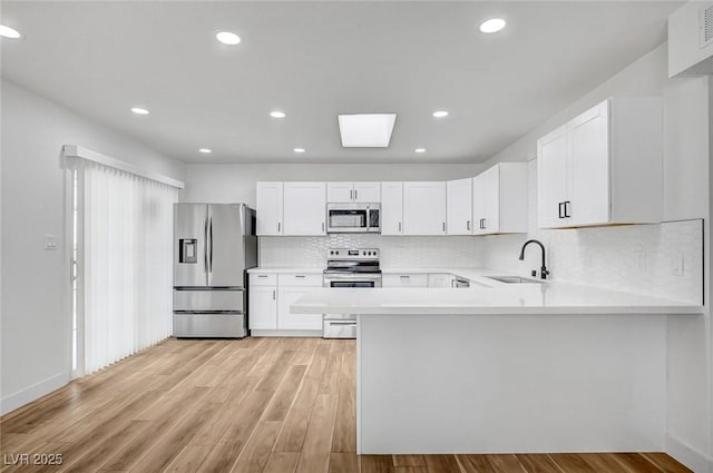 kitchen with white cabinetry, stainless steel appliances, kitchen peninsula, and sink