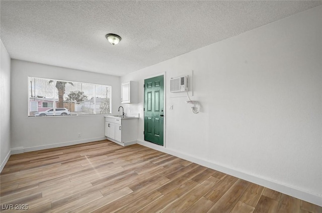 spare room with sink, light hardwood / wood-style floors, a wall unit AC, and a textured ceiling