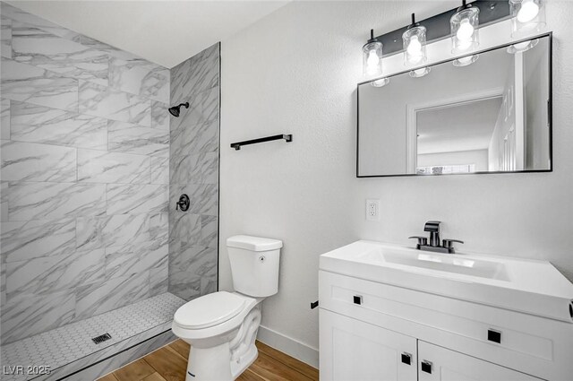 bathroom with vanity, wood-type flooring, a tile shower, and toilet