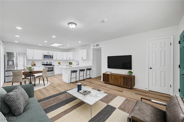 living room featuring a skylight, sink, and light hardwood / wood-style flooring