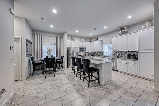 kitchen featuring stainless steel appliances, a kitchen island with sink, a breakfast bar area, and white cabinets