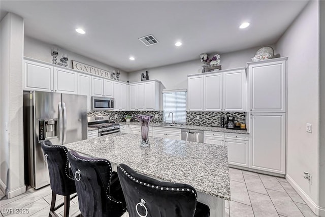 kitchen featuring stainless steel appliances, light stone countertops, a kitchen island, and a kitchen breakfast bar