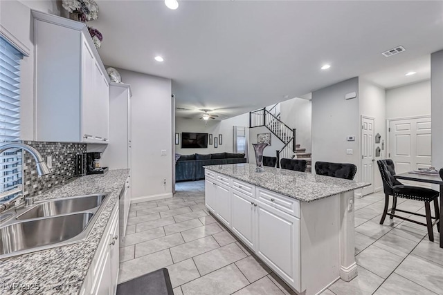 kitchen with white cabinetry, sink, a kitchen breakfast bar, and light stone countertops