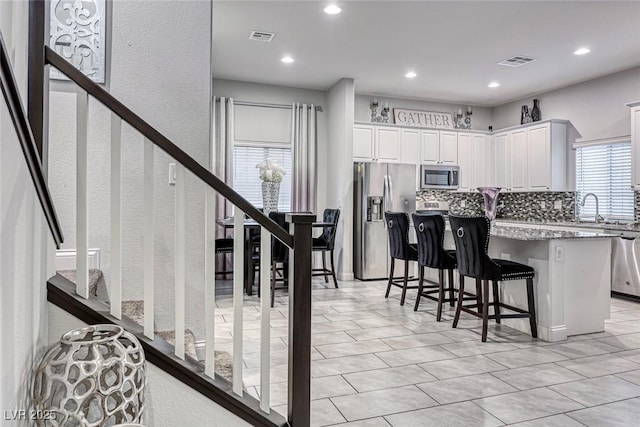 kitchen with appliances with stainless steel finishes, a center island, tasteful backsplash, white cabinets, and a kitchen bar