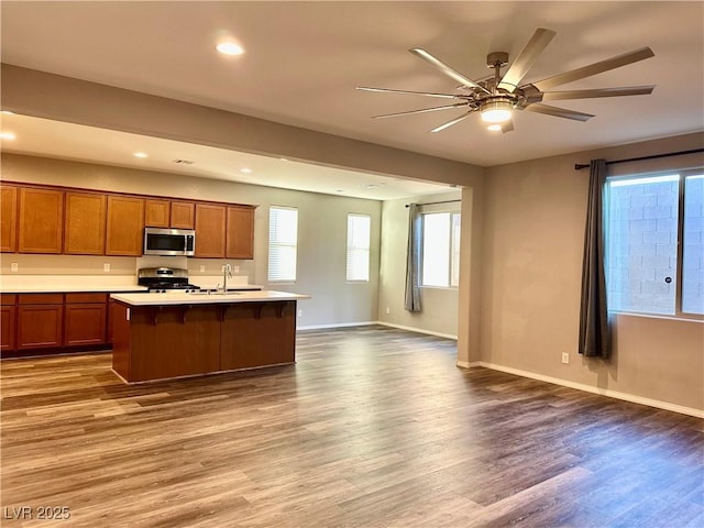 kitchen with sink, ceiling fan, appliances with stainless steel finishes, hardwood / wood-style floors, and a center island with sink