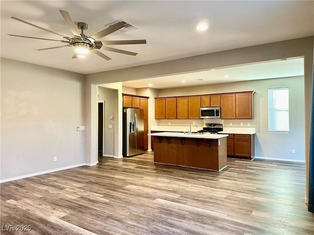 kitchen with sink, ceiling fan, stainless steel appliances, wood-type flooring, and an island with sink