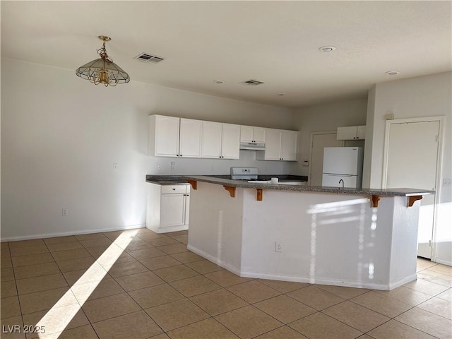 kitchen featuring white refrigerator, stove, white cabinets, and a kitchen breakfast bar