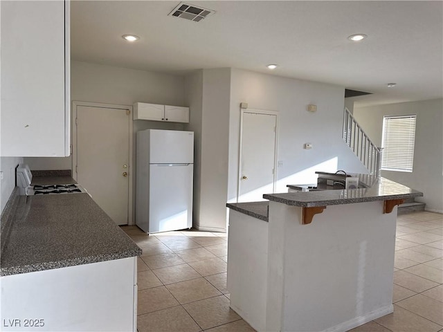 kitchen featuring light tile patterned flooring, a breakfast bar, range, white fridge, and white cabinets