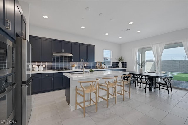 kitchen with sink, a breakfast bar, stainless steel appliances, a center island with sink, and decorative backsplash