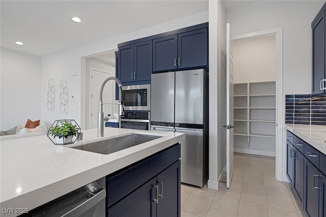 kitchen with sink, blue cabinetry, light tile patterned flooring, and appliances with stainless steel finishes