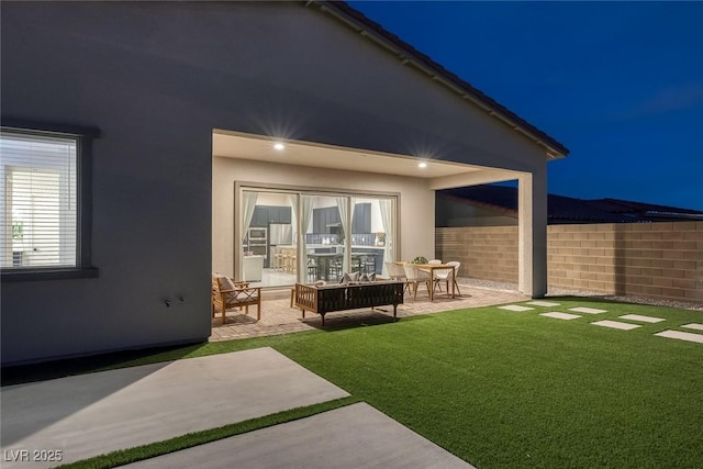 back house at night featuring a yard, outdoor lounge area, and a patio