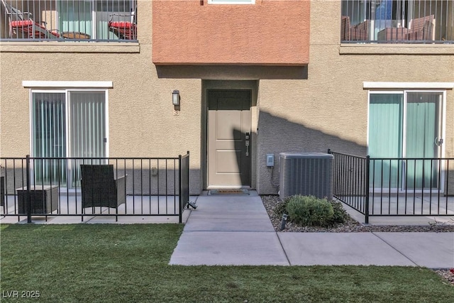 entrance to property featuring a lawn, cooling unit, and stucco siding