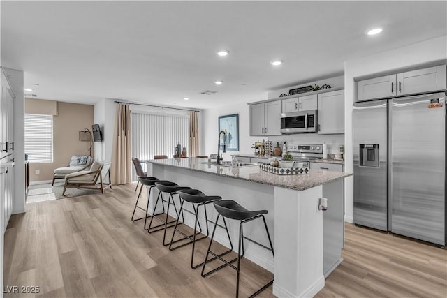 kitchen featuring appliances with stainless steel finishes, sink, a kitchen bar, a kitchen island with sink, and light stone countertops