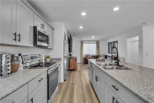 kitchen with light stone counters, appliances with stainless steel finishes, light hardwood / wood-style floors, and sink