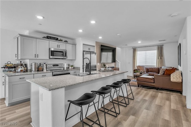 kitchen featuring light stone counters, a breakfast bar area, stainless steel appliances, a sink, and light wood finished floors