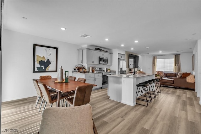 kitchen with visible vents, light wood-style flooring, a breakfast bar area, open floor plan, and stainless steel appliances