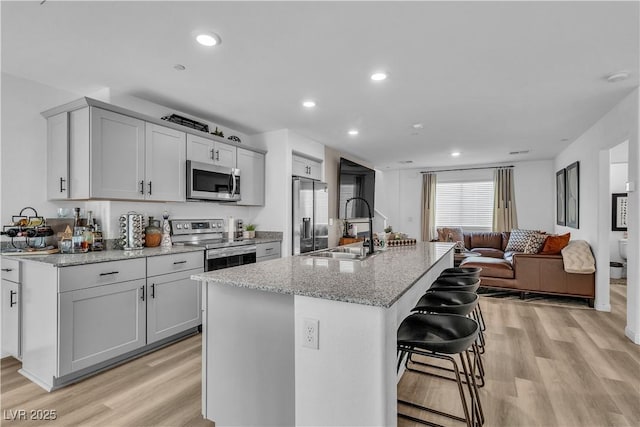 kitchen with stainless steel appliances, light wood finished floors, a kitchen bar, and a sink