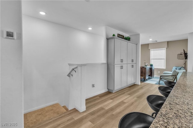 kitchen featuring light wood-style flooring, recessed lighting, white cabinets, baseboards, and light stone countertops