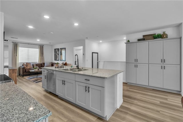 kitchen featuring light wood finished floors, a center island with sink, dishwasher, open floor plan, and a sink