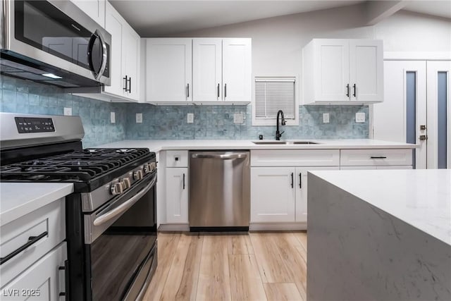 kitchen featuring sink, vaulted ceiling, stainless steel appliances, light hardwood / wood-style floors, and white cabinets