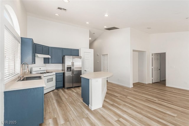 kitchen with a kitchen island, high vaulted ceiling, white gas range, sink, and stainless steel fridge