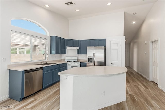 kitchen featuring sink, a towering ceiling, stainless steel appliances, a center island, and blue cabinets