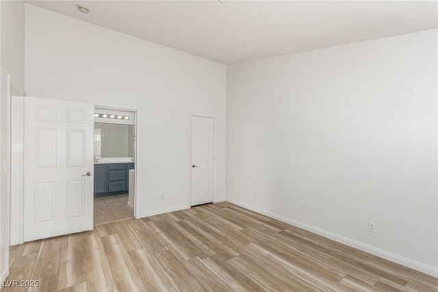 unfurnished bedroom with a towering ceiling, ensuite bathroom, and light hardwood / wood-style flooring